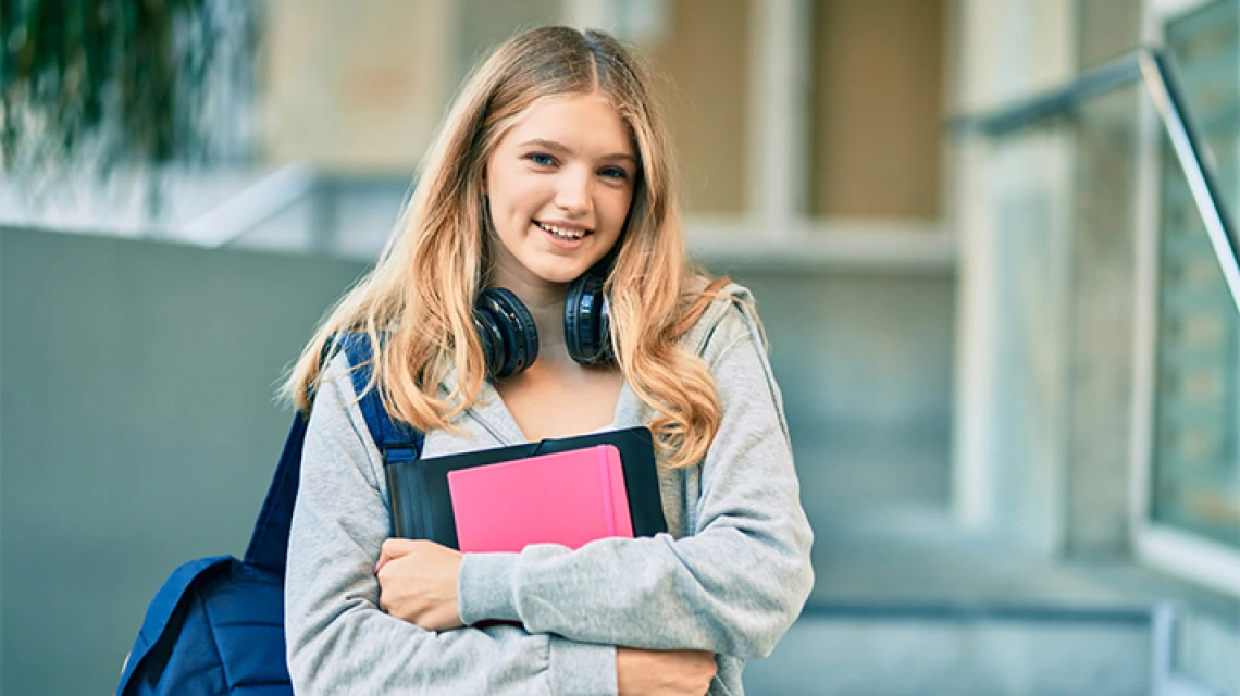 Student smiling and holding school materials outside